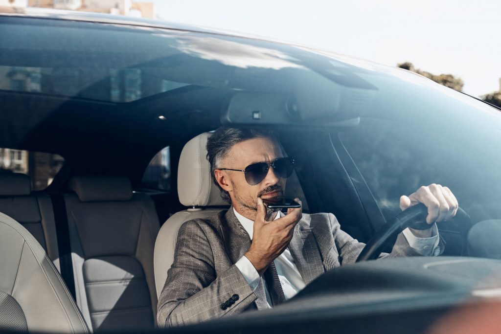 Üzletember szürke öltönyben speech to text alkalmazást használ autójában ülve
