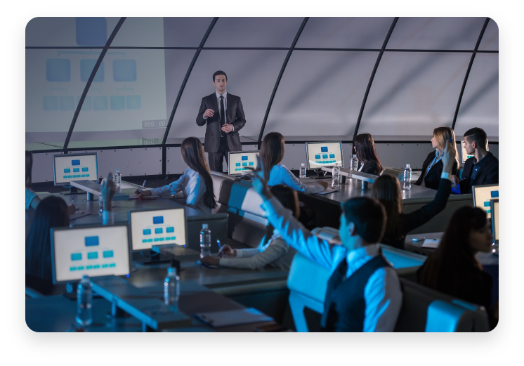 Egy férfi prezentál egy üzleti megbeszélésen a kollégái előtt, miközben az elhangzott szöveg valós időben feliratozva van a monitorokon.