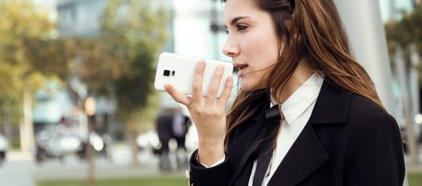 Üzletasszony voice to text alkalmazást használ a telefonján, miközben kint van a szabadban